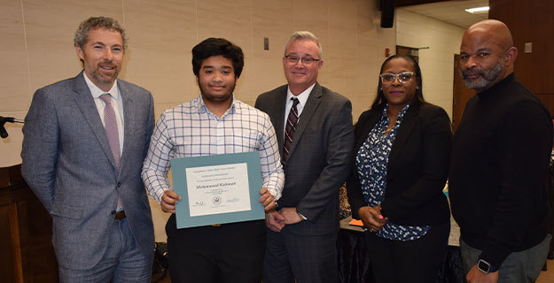 Student holding a certifcate and smiling with BOE members