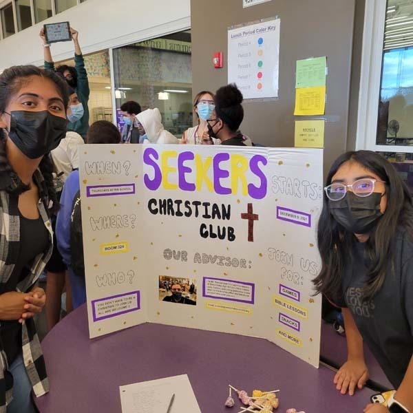 Students next to Seekers Christianity Club Poster