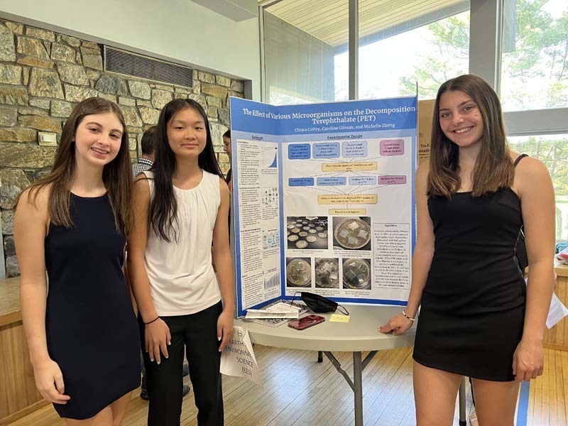 Three students stand next to a research project