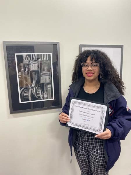 A student standing in front of art and holding a certificate while smiling