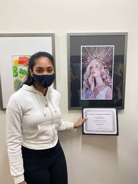 A student standing in front of art and holding a certificate while smiling